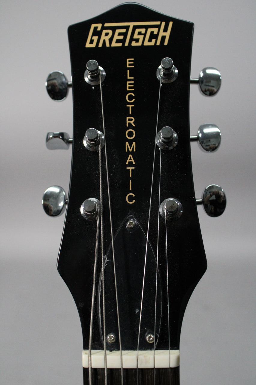 Close-up of the black headstock with six chrome tuners, showing the white nut and a few light scratches on the finish.