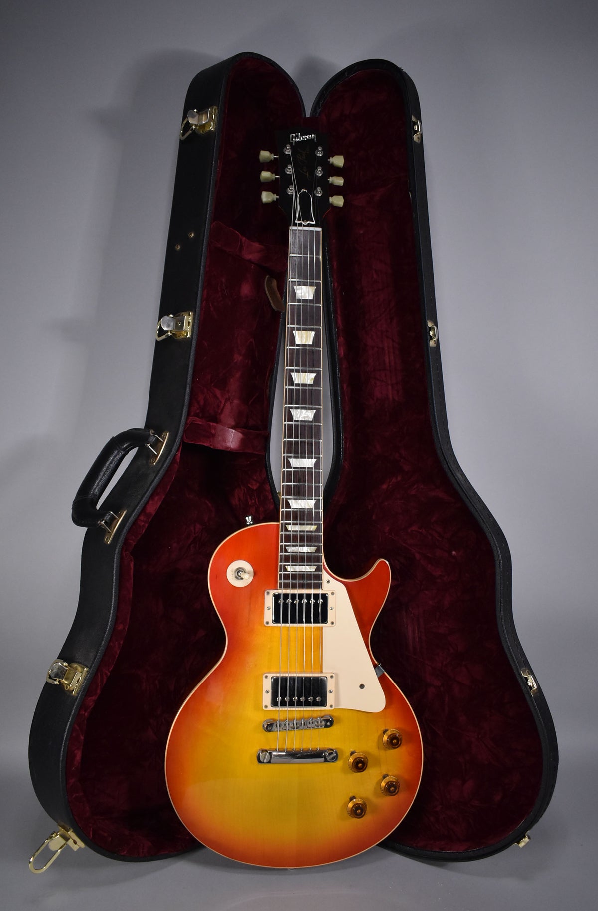 Full-length view of a cherry sunburst electric guitar with cream binding, standing in its open, red-lined hard case.