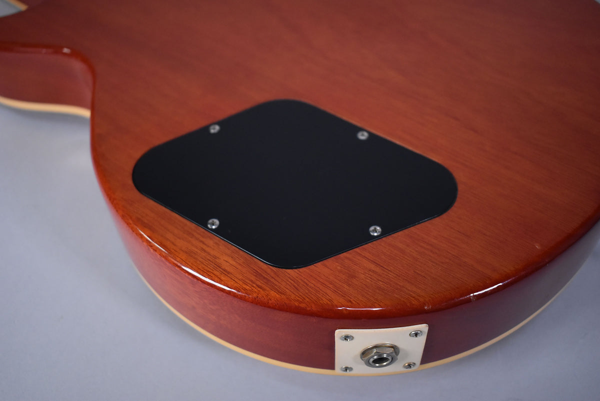 The lower back of the cherry sunburst guitar shows a black control cavity cover and a cream output jack plate with minor wear.
