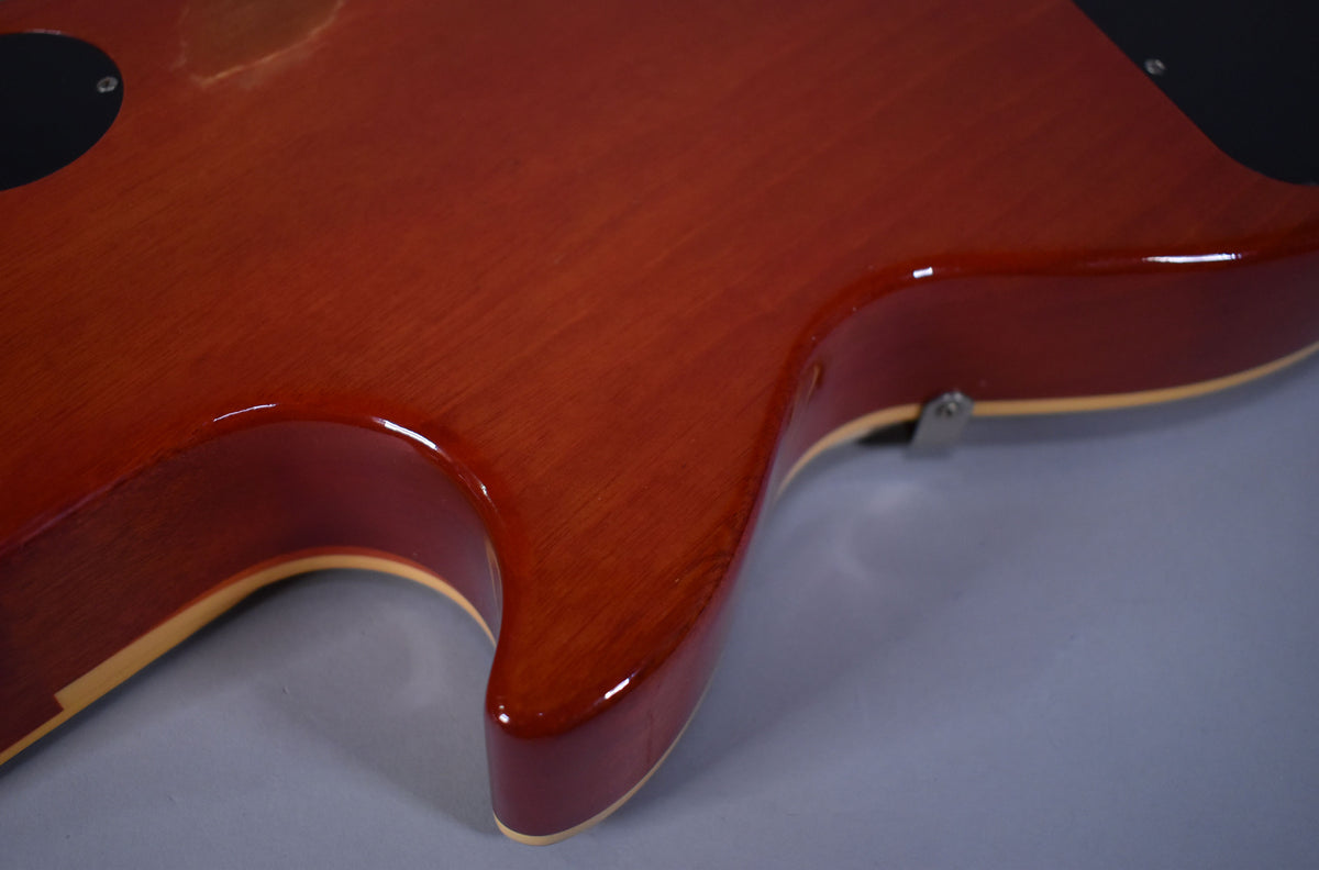 The guitar's lower bout and cutaway are shown from the back, revealing a cherry sunburst finish with a worn patch near the neck joint.