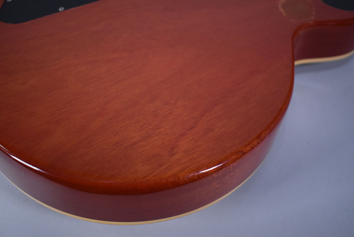 Close-up of the guitar's cherry sunburst back, showing wood grain, a worn patch near the top edge, and cream binding.