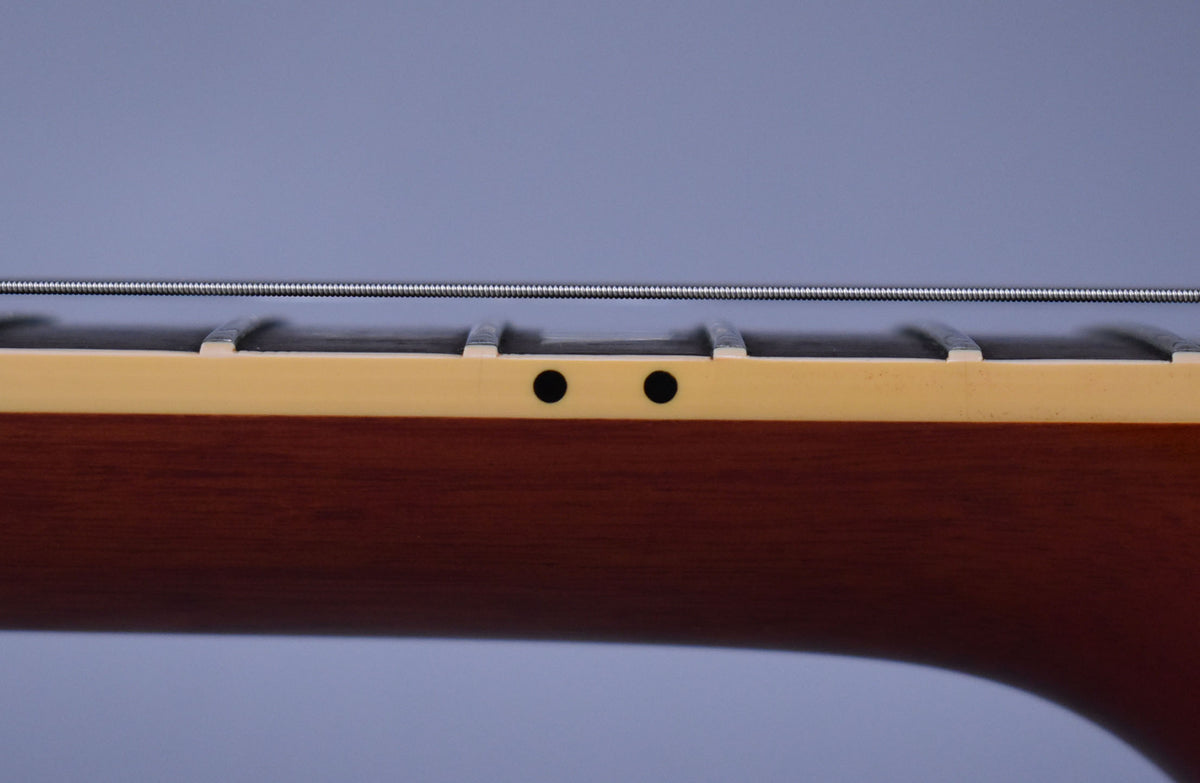 Close-up of the guitar neck's side, showing the dark brown wood, cream binding, two black side dots, and four frets with strings above.
