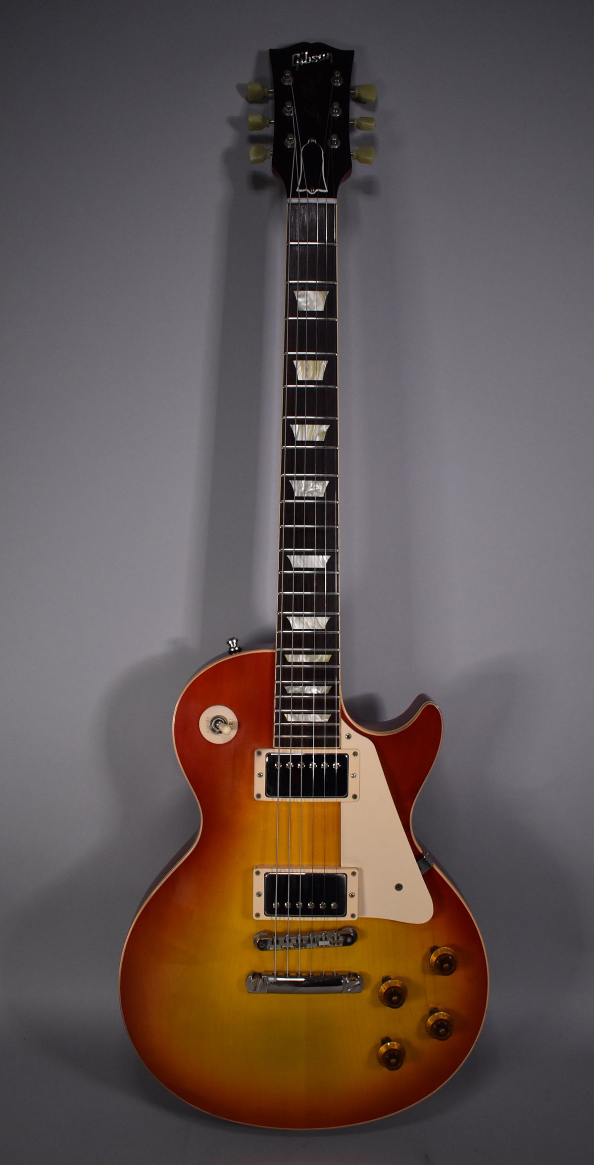 Full-length view of a cherry sunburst guitar with a dark headstock, trapezoid inlays, cream pickguard, and gold knobs.