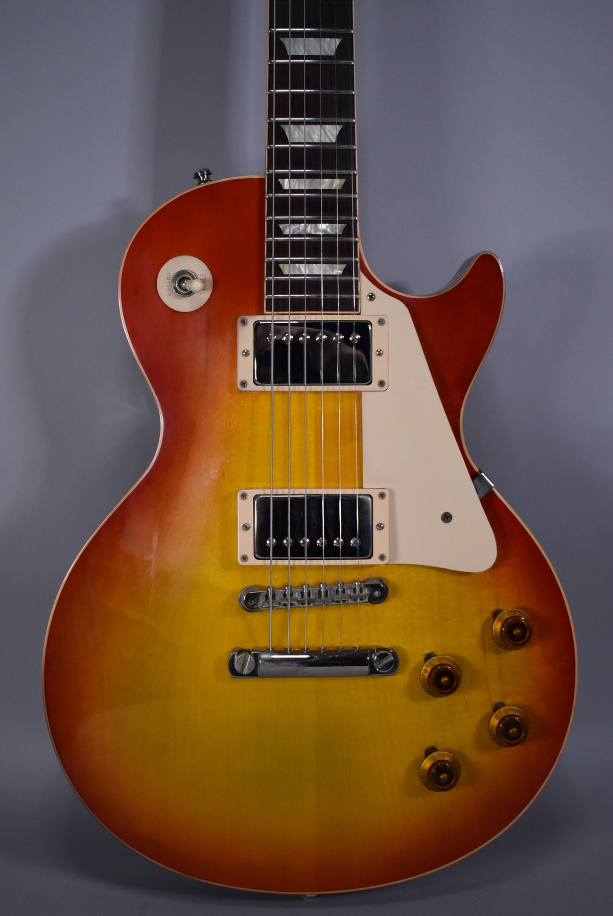 A cherry sunburst Les Paul guitar, showing the body, pickups, bridge, controls, and part of the neck with trapezoid inlays.