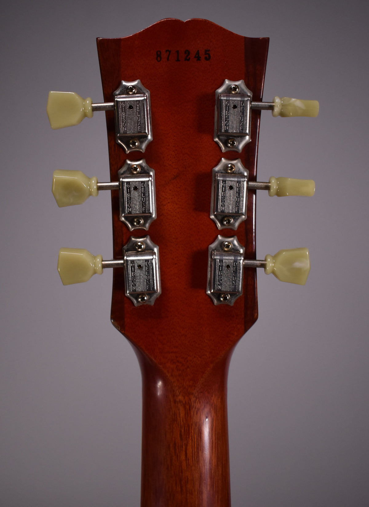 Rear view of the guitar's headstock and upper neck, showing six cream-colored tuning pegs and chrome tuners on a cherry-stained finish.