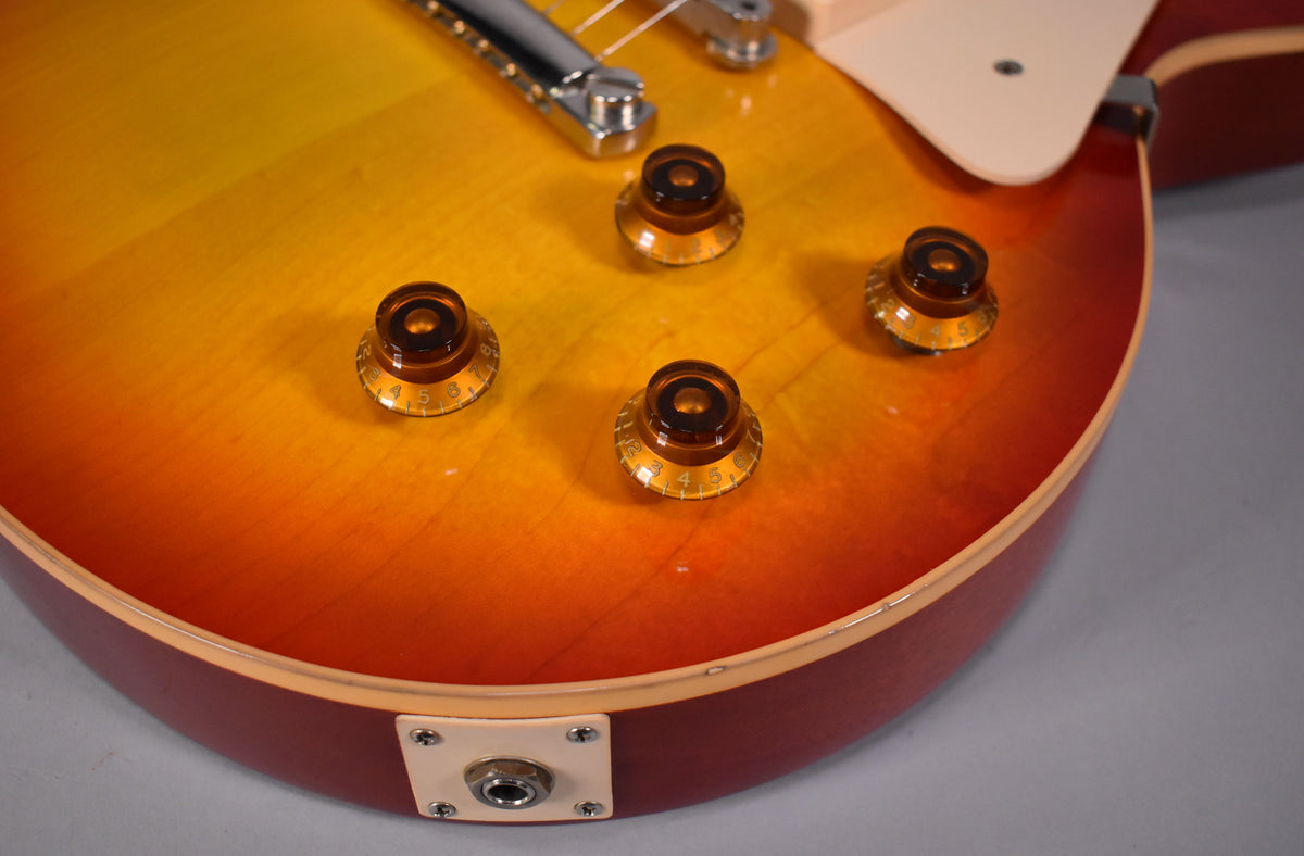 Close-up of the cherry sunburst body, showing four amber top hat knobs, output jack, and light finish checking on the binding.