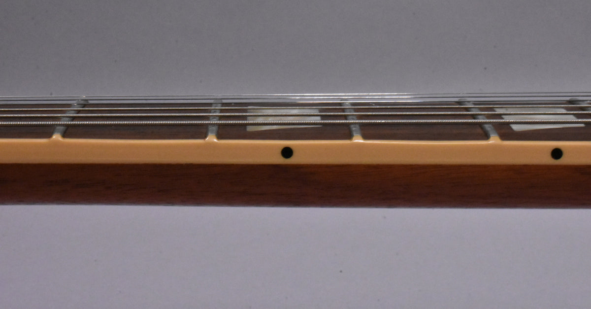 Close-up of the guitar's fretboard, showing the light-colored binding, dark wood, and trapezoid inlays with side dots.