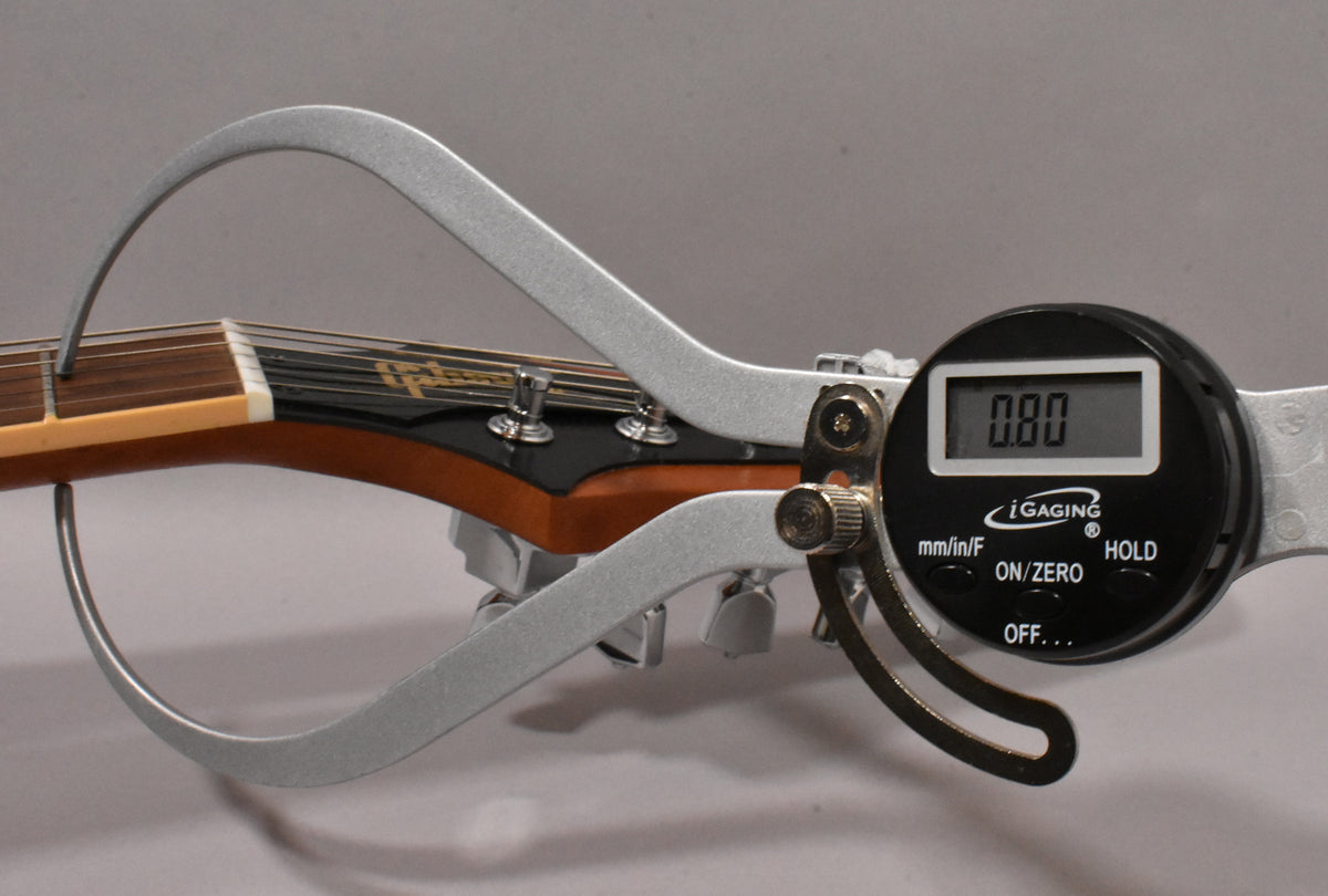 A digital caliper measures the guitar's neck relief, showing 0.80, with the headstock and tuning pegs visible.