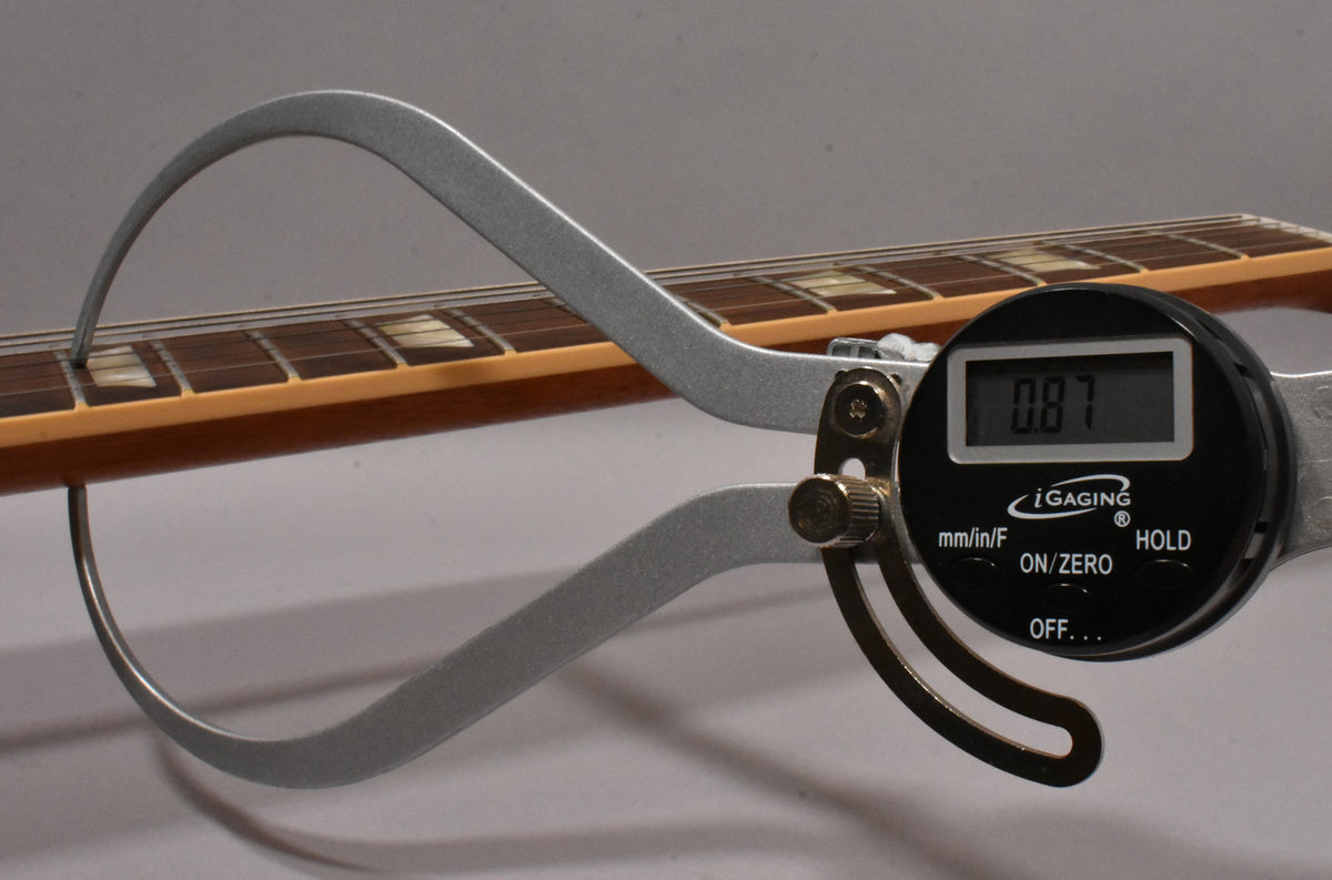 A digital caliper measures the guitar's fret height at 0.87mm, showing the rosewood fretboard with trapezoid inlays and cream binding.