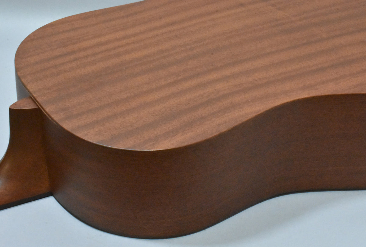 The lower bout of a mahogany acoustic guitar, showing the natural wood grain and a smooth, matte finish.