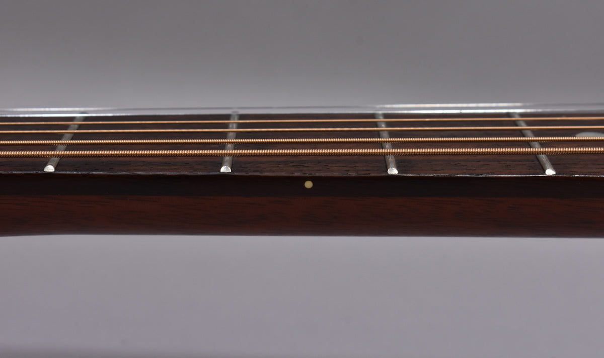 Close-up of the dark brown fretboard and neck, showing four bronze strings, silver frets, and a single light dot inlay.