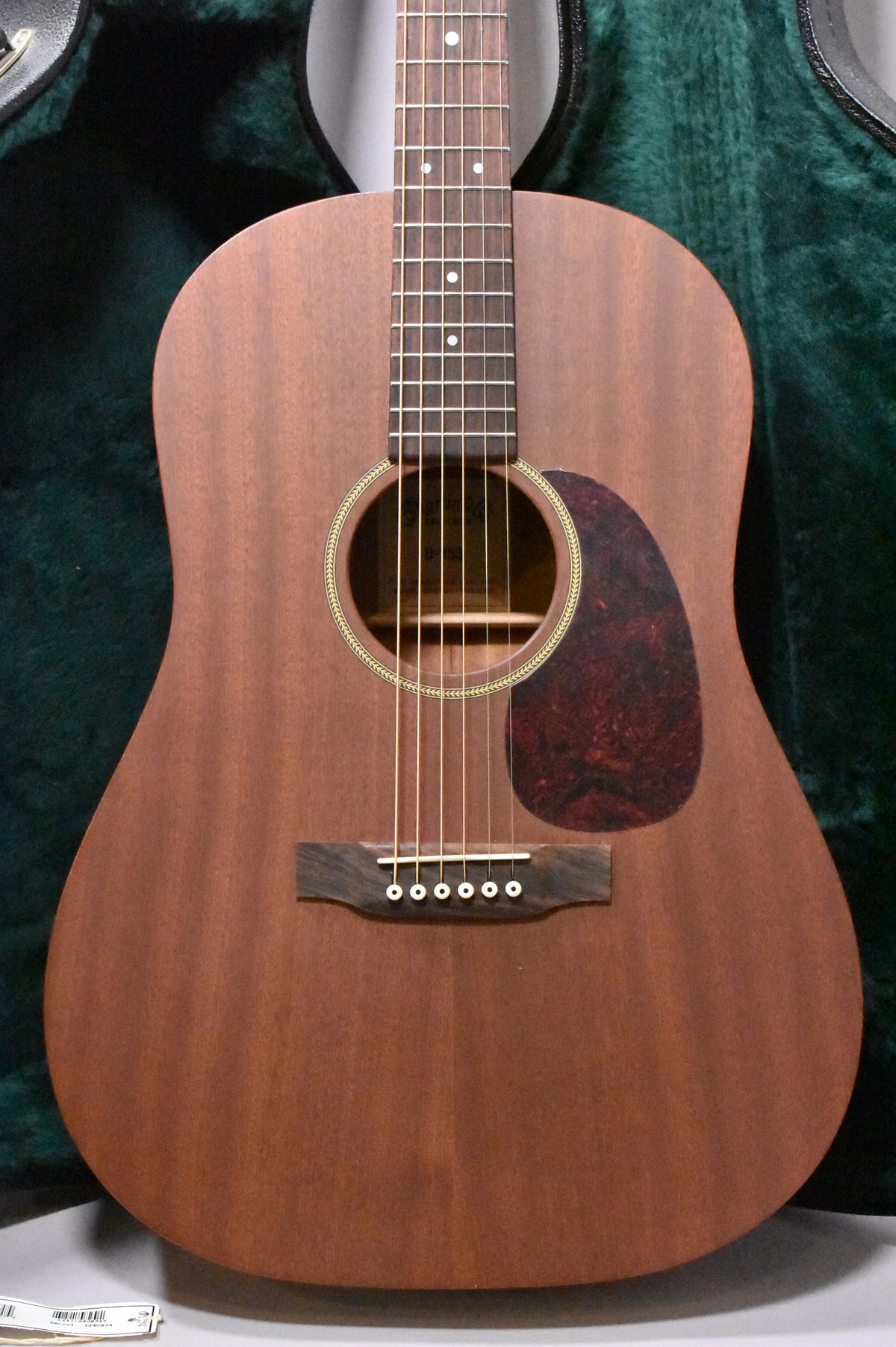 The acoustic guitar's body and fretboard are framed, showing a matte mahogany finish, tortoise pickguard, and simple rosette.