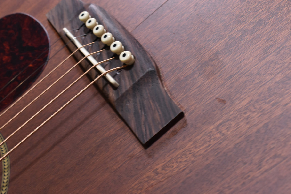 Close-up of the mahogany body and dark wood bridge with six cream pins, showing a small dark mark on the body.