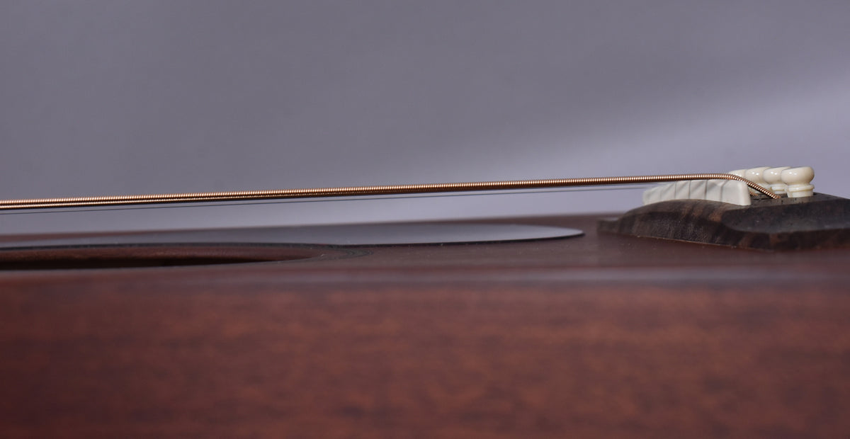 Extreme close-up of the guitar's dark mahogany body and bridge, showing the saddle and six cream-colored bridge pins with a string passing over.