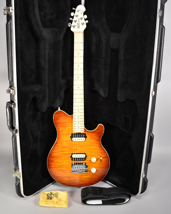 Full-length view of a sunburst electric guitar with a flamed maple top, maple fretboard, two humbuckers, and a tremolo bridge, in its open hard case.