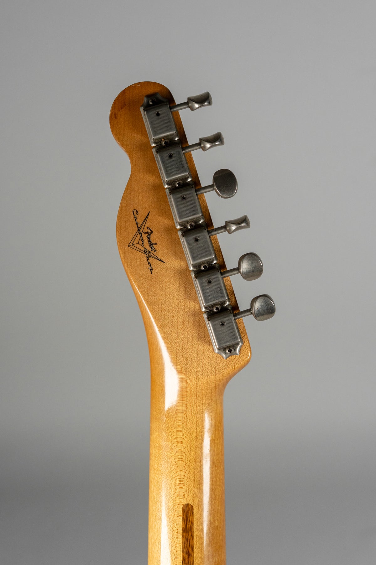 The light-colored maple headstock and neck are viewed from behind, showing six aged, rectangular tuners and light wear.