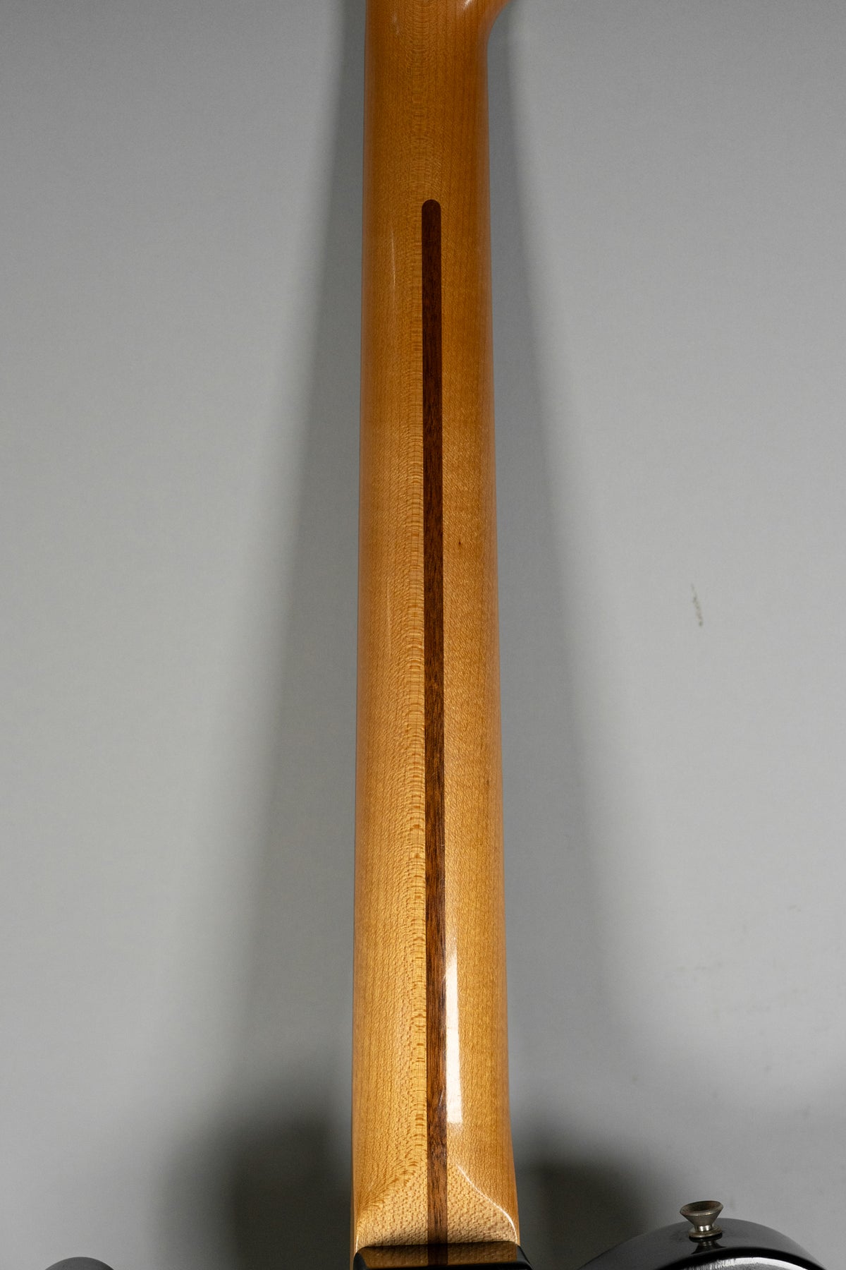 The back of a light wood guitar neck with a dark stripe down the center, showing wood grain and a glossy finish.