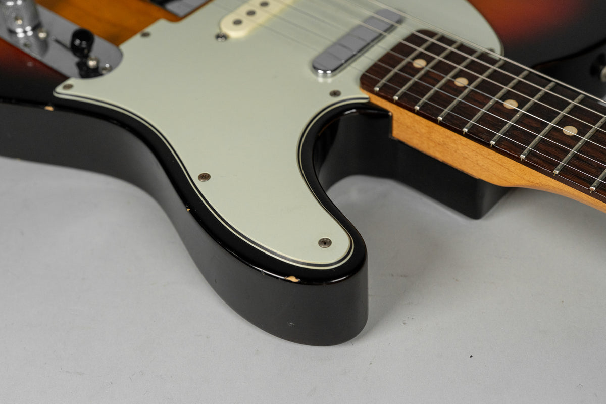Close-up of the lower bout, showing the sunburst finish, cream pickguard, and a chip on the black edge of the body.