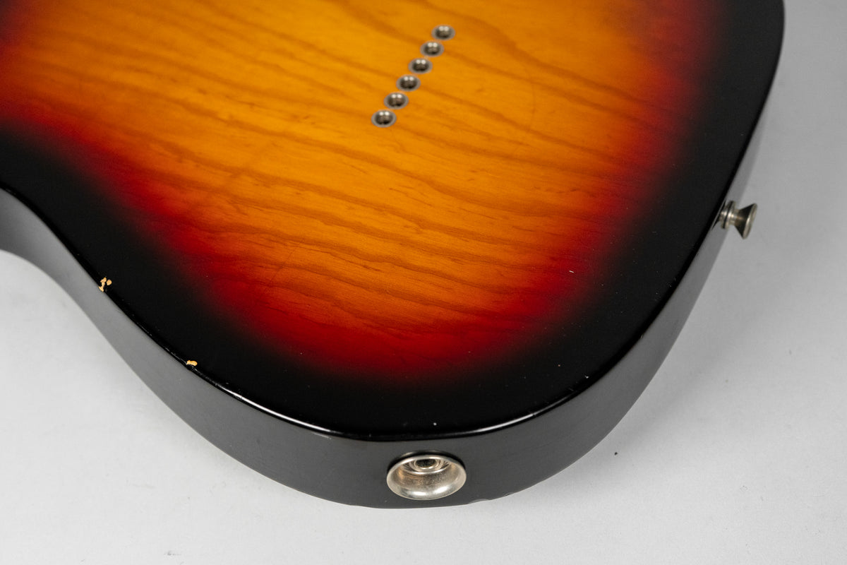 The lower bout of a sunburst guitar body, showing string-through ferrules, output jack, strap button, and finish wear.