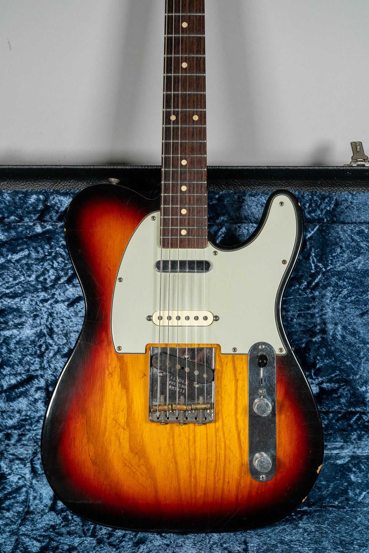 Sunburst Telecaster body and lower neck, showing a cream pickguard, chrome bridge, control plate, and visible finish wear.