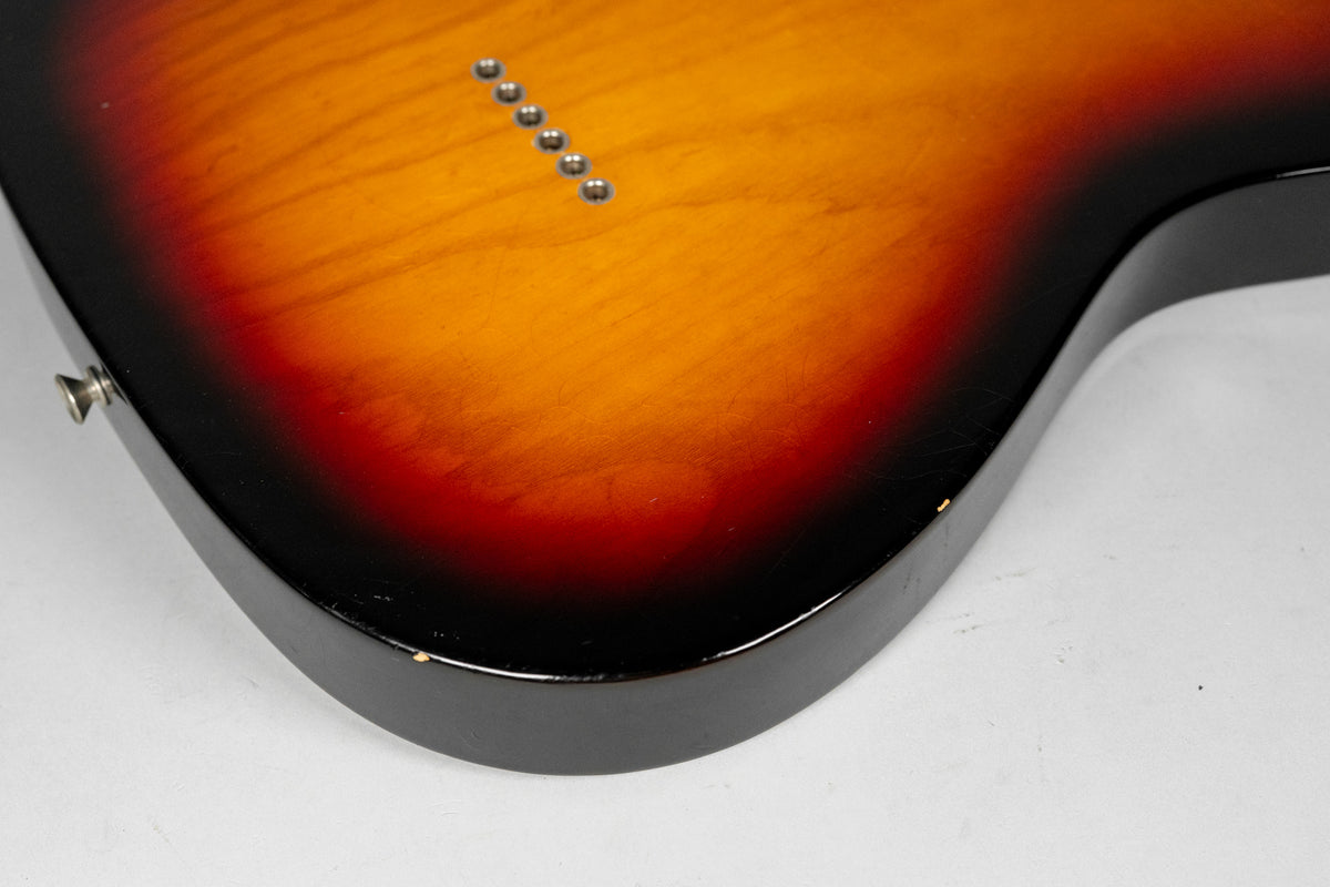 The back of a sunburst guitar body, showing six string-through-body ferrules and light wear on the black edge.