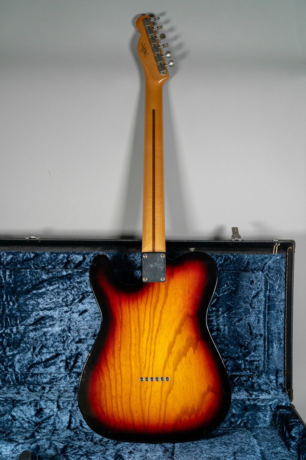 Full rear view of a sunburst Telecaster with a maple neck, showing six string ferrules and a worn neck plate, resting in a blue velvet case.