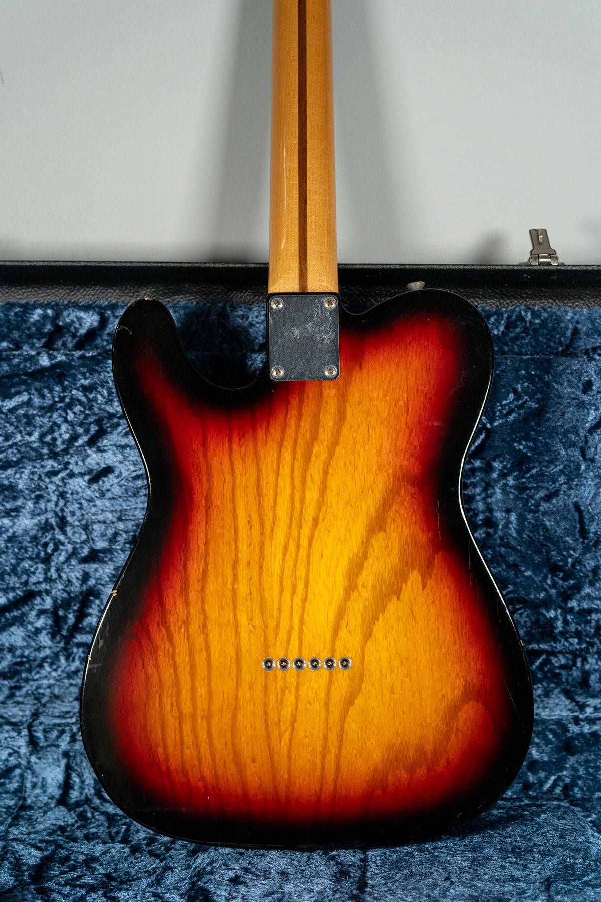 Rear view of a sunburst Telecaster body with a maple neck, showing string-through-body ferrules and a worn neck plate.
