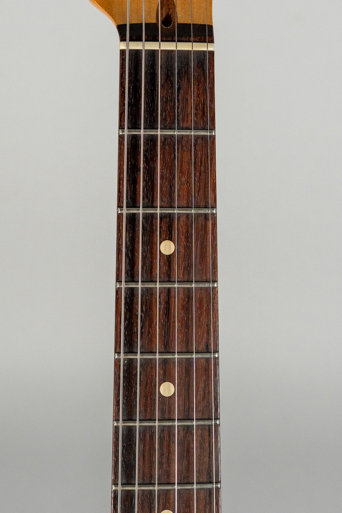 Close-up of the dark rosewood fretboard with light circular inlays, showing light wear on the frets and a bone nut.