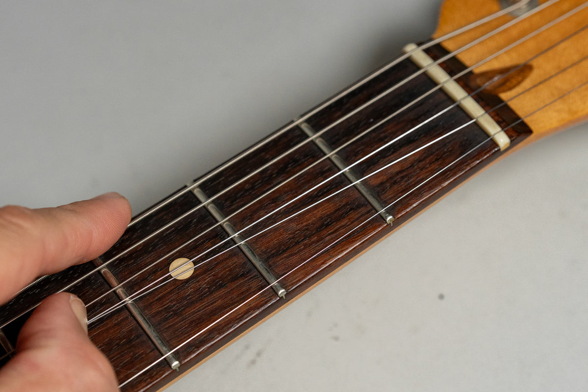 Close-up of the dark rosewood fretboard with a single light dot inlay, showing light wear on the frets and a bone nut.