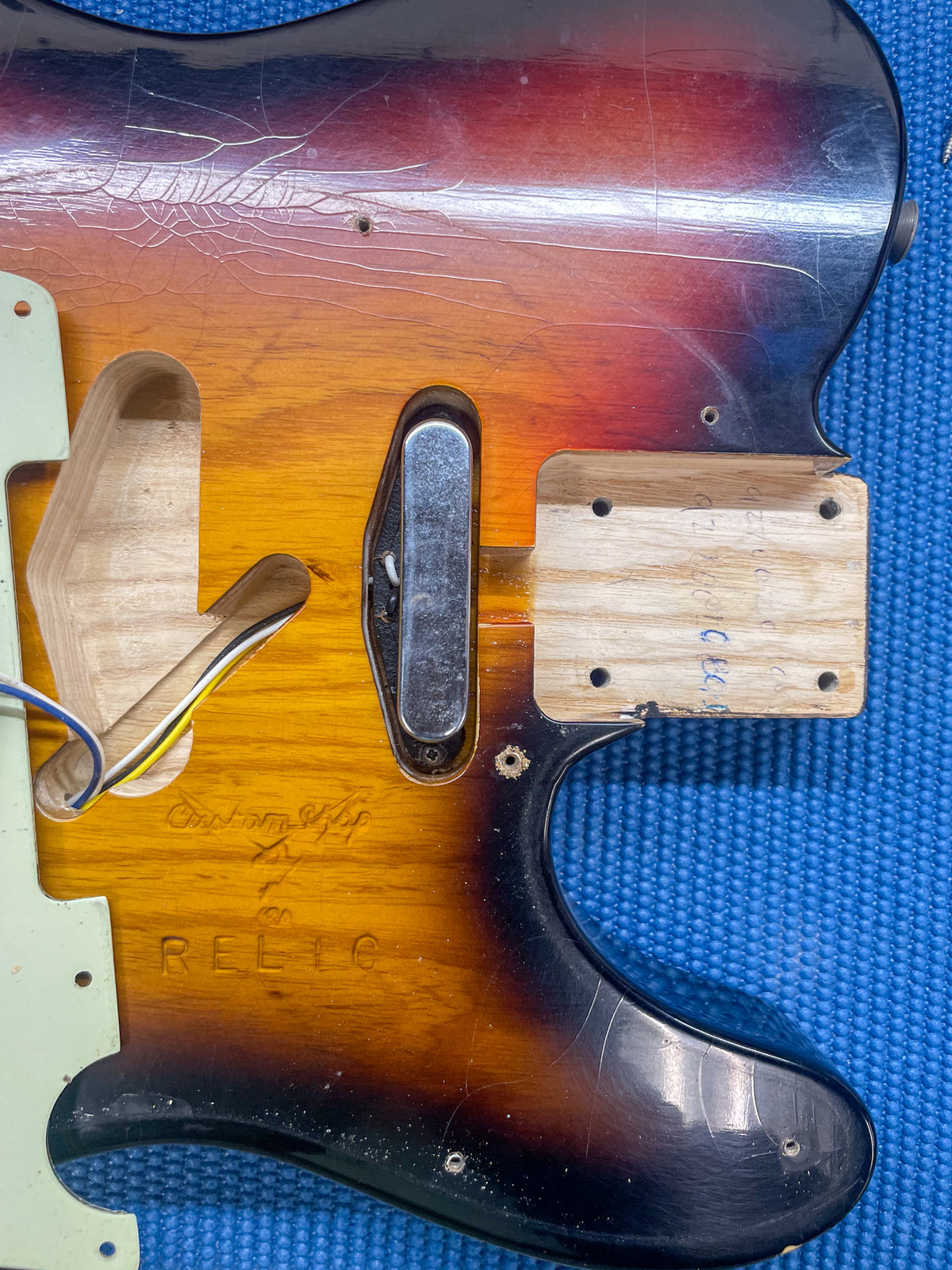 Close-up of the sunburst body with pickguard removed, showing a chrome bridge pickup, neck pocket, and extensive finish checking.