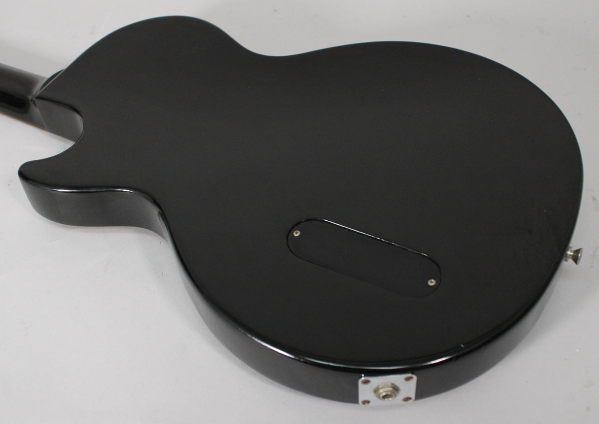 Rear view of a glossy black Les Paul Jr. body, showing the control cavity cover and chrome output jack.