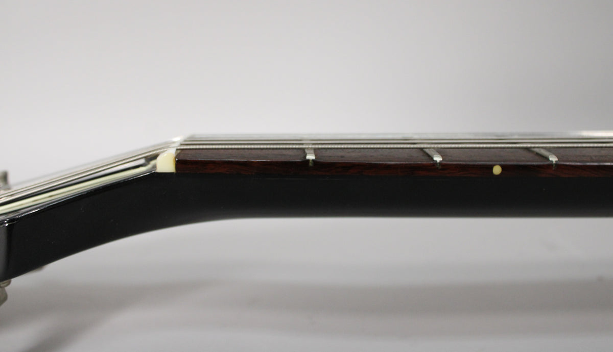 Close-up of the ebony neck and dark rosewood fretboard, showing the nut, first three frets, and a single dot inlay.