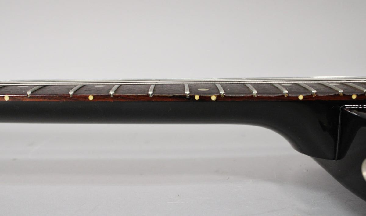 Side view of the ebony guitar neck and dark rosewood fretboard with dot inlays, showing some wear and chipping along the fretboard edge.