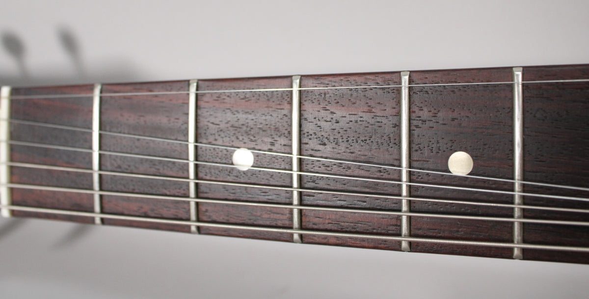 Close-up of the dark rosewood fretboard with six strings, showing white dot inlays at the 5th and 7th frets.