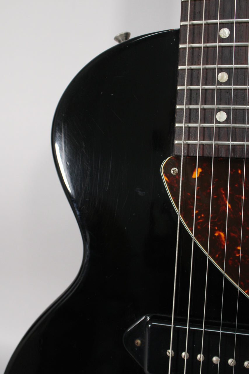 Close-up of the ebony body, showing heavy pick scratches on the upper bout and a tortoiseshell pickguard with a single P90 pickup.