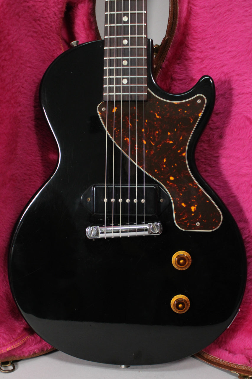 Full view of the glossy black body, with a tortoiseshell pickguard, single P90 pickup, chrome wraparound bridge, and amber knobs.