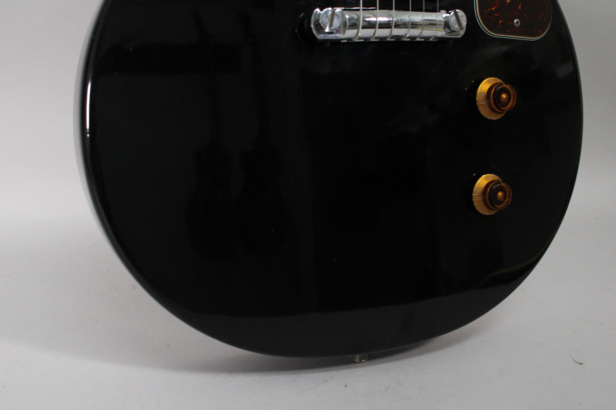 Close-up of the glossy black body, showing the chrome bridge, tortoiseshell pickguard, and two amber control knobs.