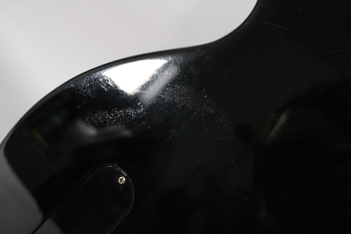 Close-up of the guitar's upper bout, showing heavy pick scratches and scuffs on the glossy black finish, with a control plate screw visible.