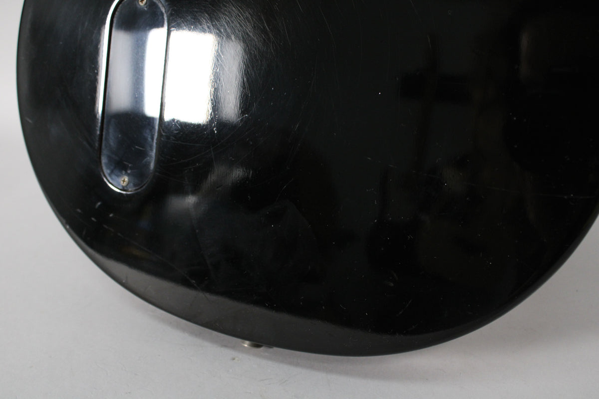 The lower back of the black guitar body shows a control cavity cover and many surface scratches and scuffs.