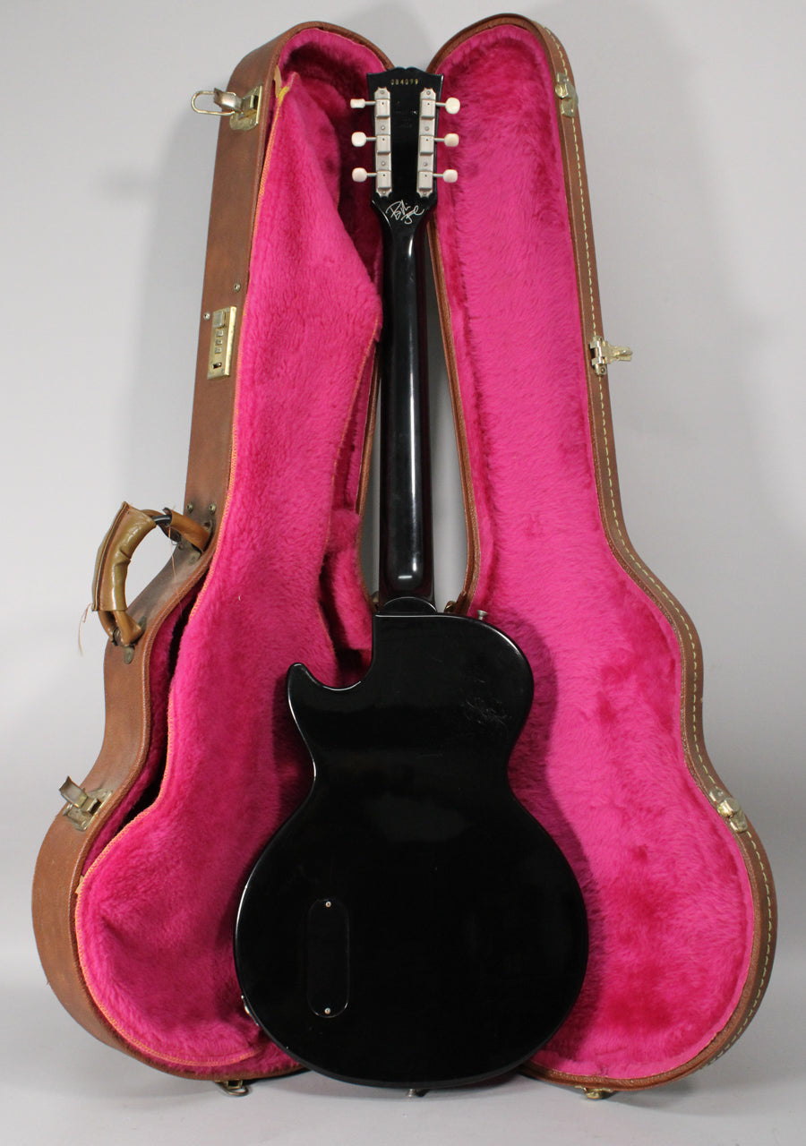 Full rear view of the glossy black Les Paul Jr. in its open brown hard case with bright pink plush lining.