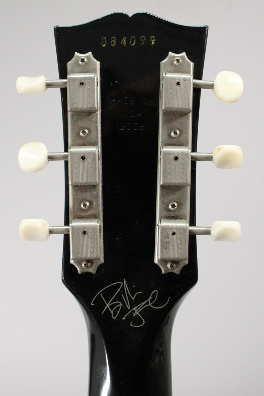 Rear view of the black headstock with six cream tuners, showing a white signature and some minor wear.