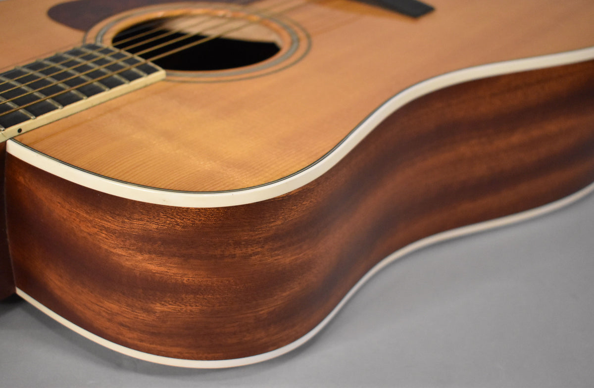 Close-up of the guitar's lower bout, showing the light natural top, dark reddish-brown sides, and white binding.