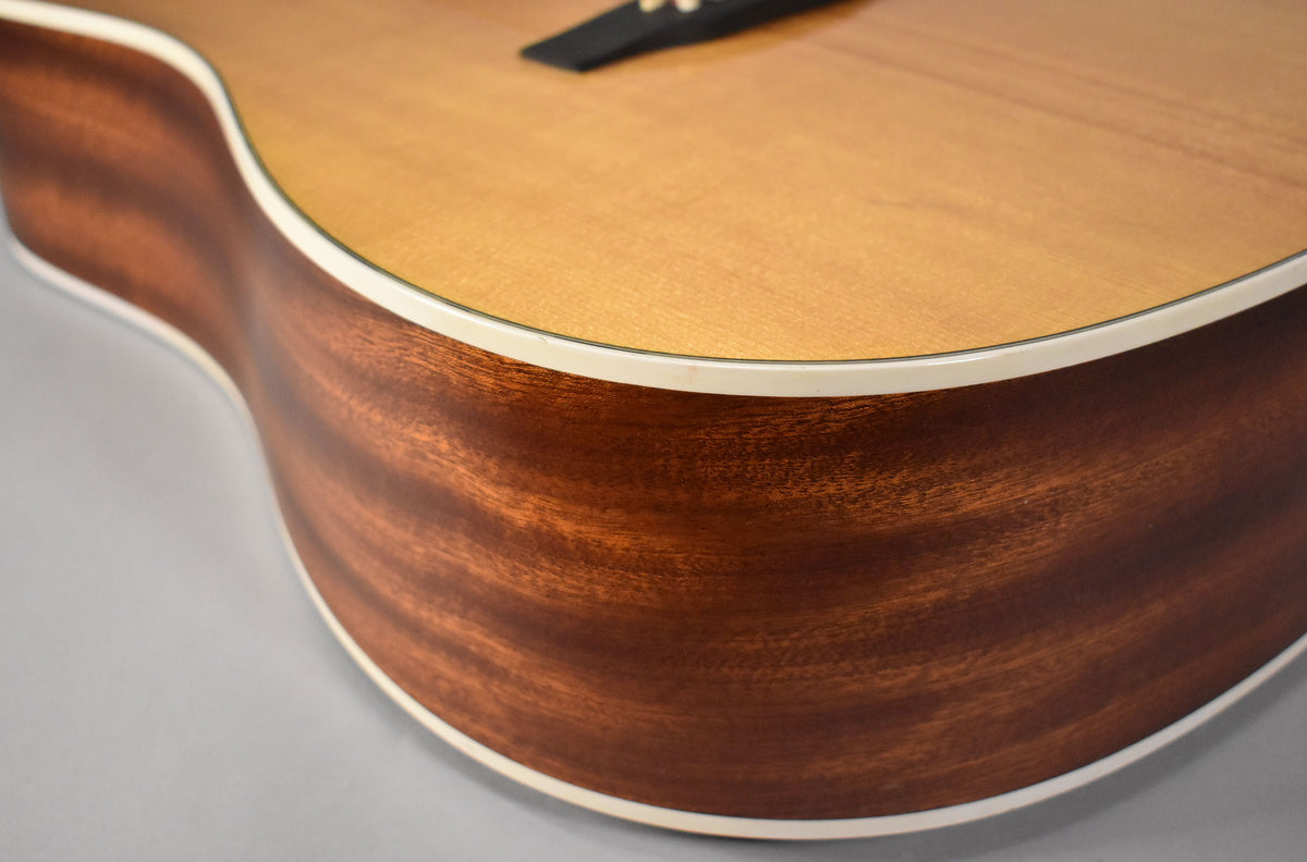 Close-up of the guitar's lower bout, showing the natural wood grain of the dark brown sides and the lighter top with white binding.