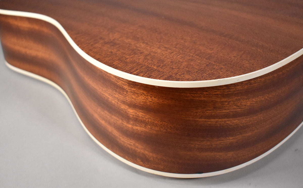 Close-up of the guitar's lower bout and side, showing the natural wood grain and white binding, with a small ding on the top edge.