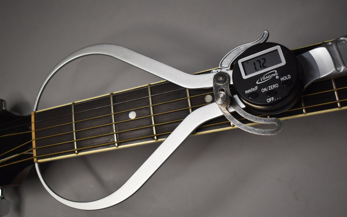A digital caliper measures the guitar's dark fretboard, showing a 1.72mm reading, with light strings and dot inlays visible.