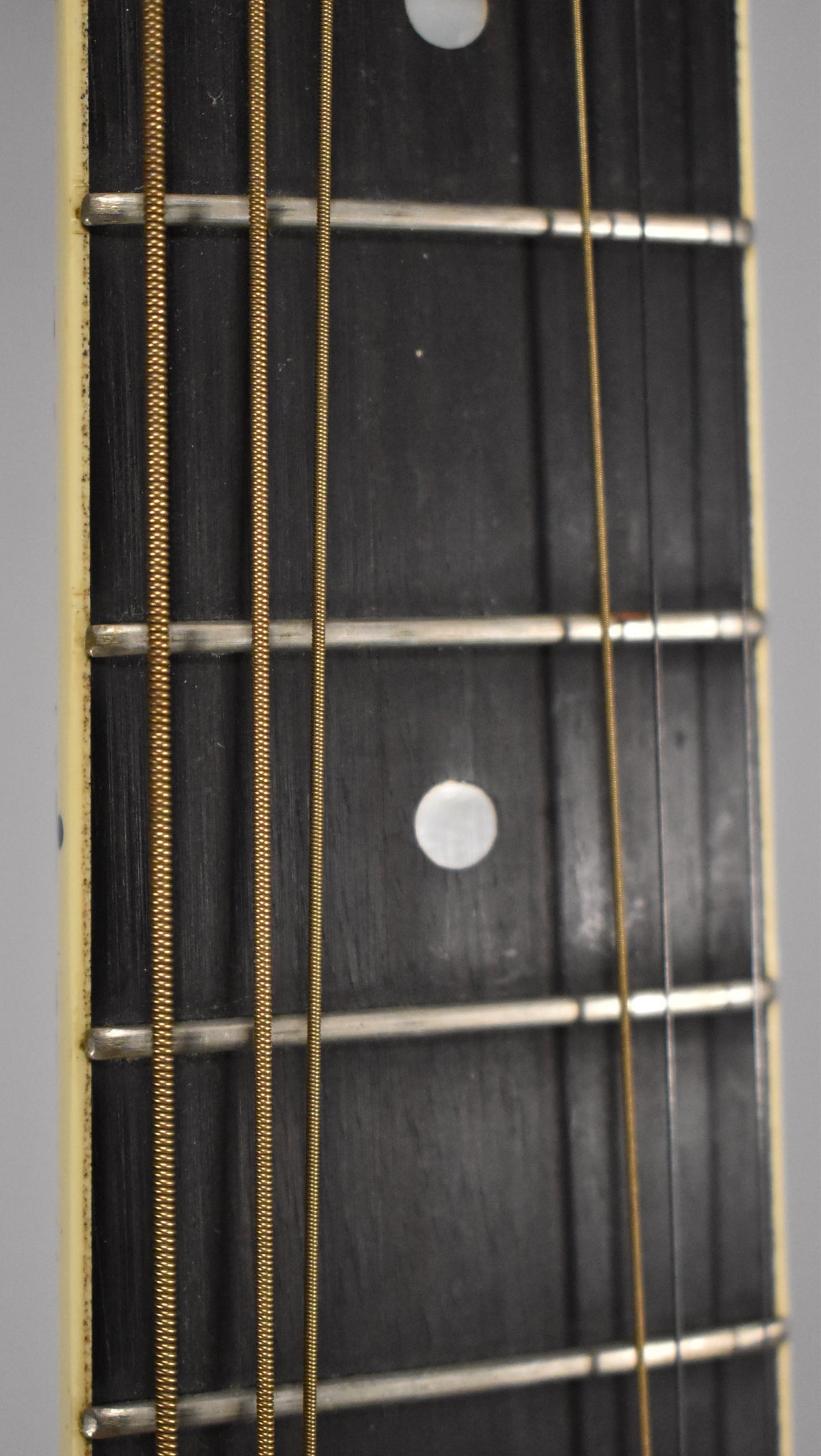 Close-up of the guitar's dark fretboard with light fret markers and metal frets, showing four bronze strings and light wear.