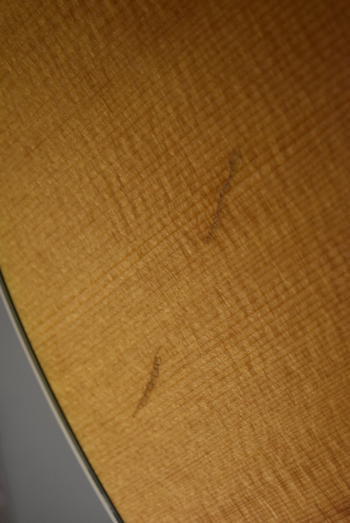 A close-up of the natural finish acoustic guitar's body, showing light wood grain and two thin, dark scuff marks.