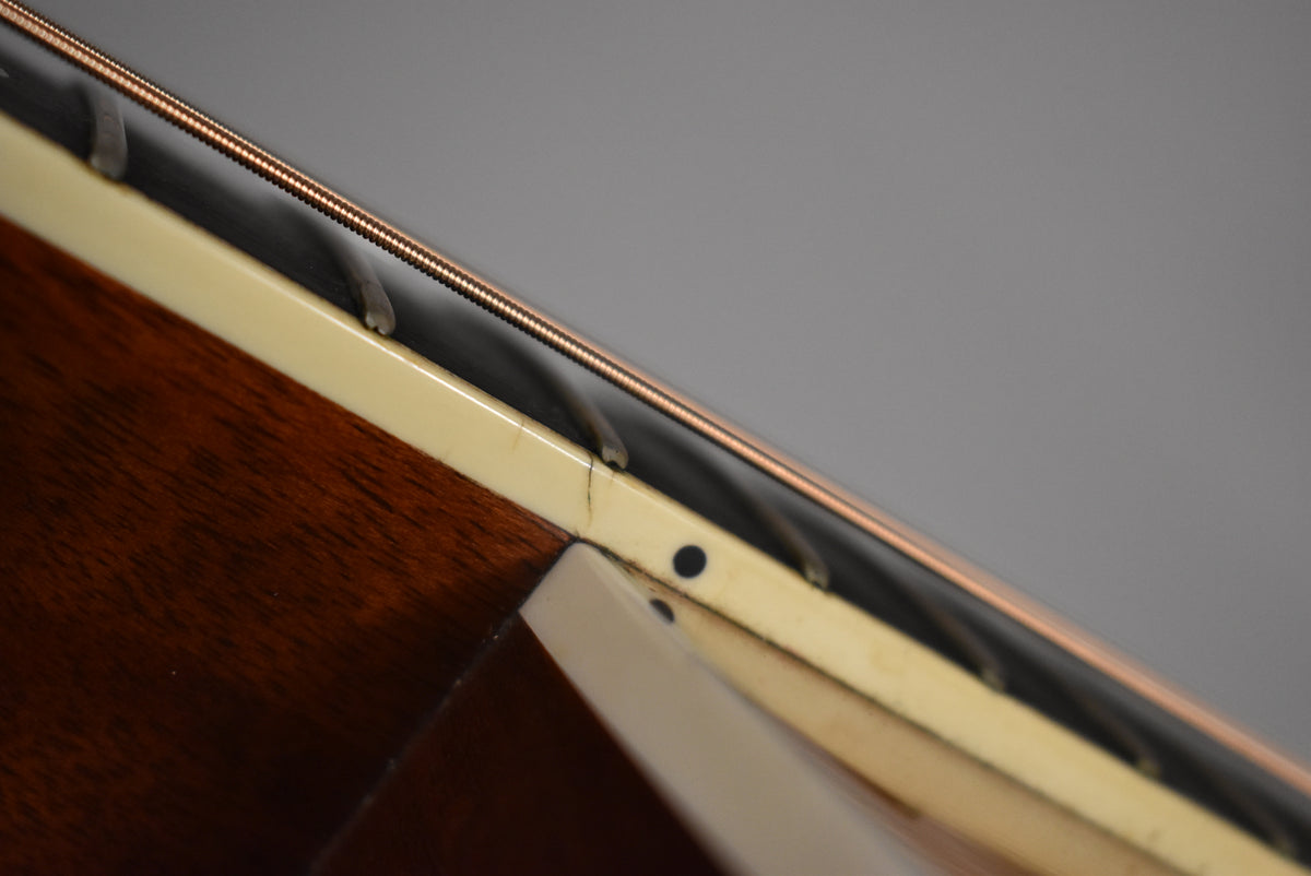 Close-up of the guitar's natural finish mahogany neck and cream binding, showing a small crack in the binding near the body joint.