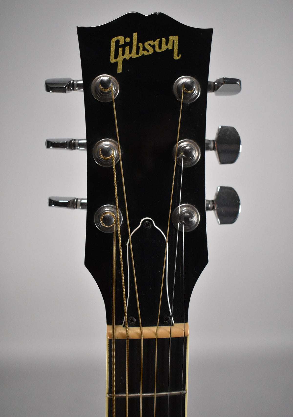 The guitar's black headstock, with gold lettering and six chrome tuners, is framed from the nut upwards.
