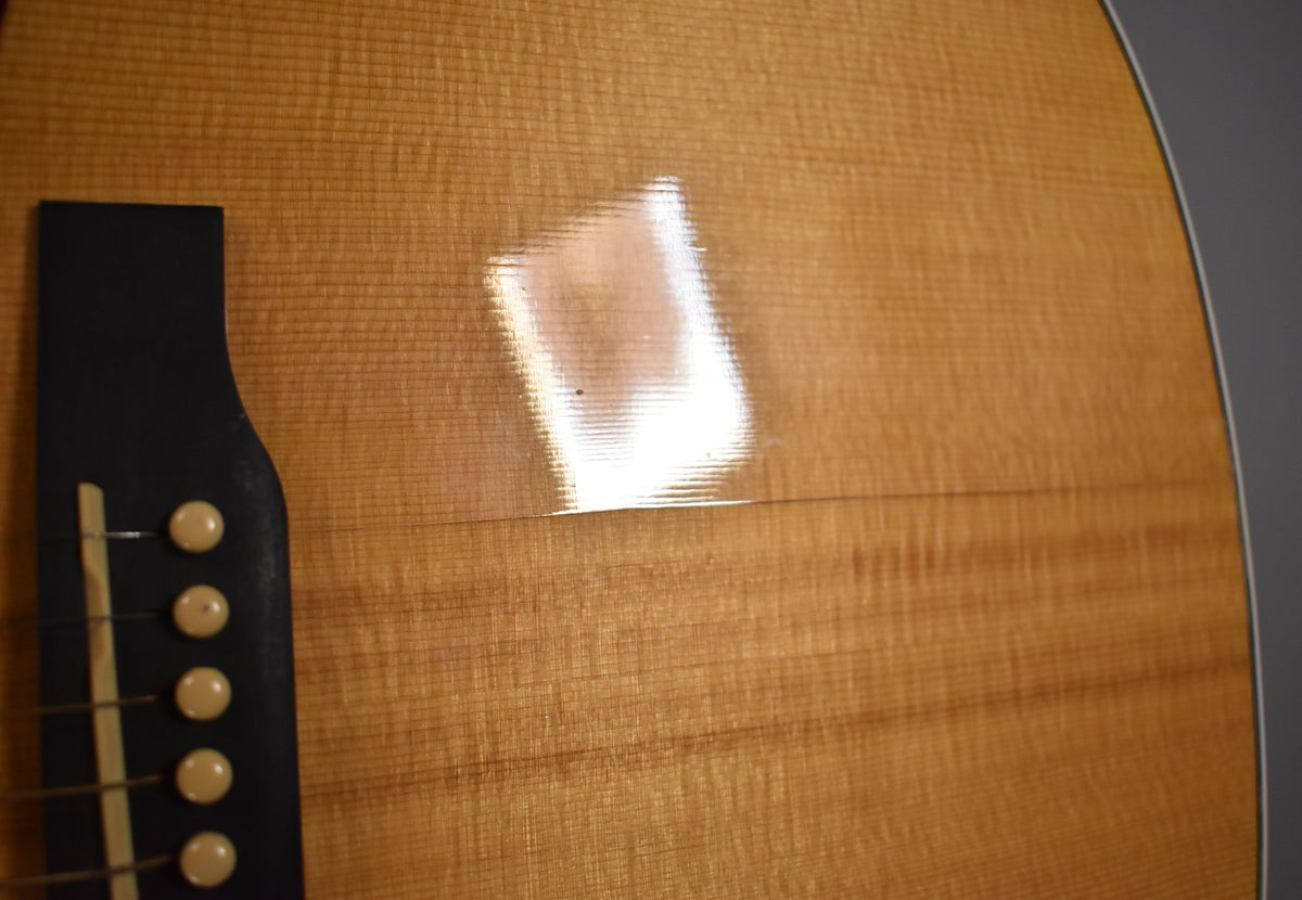 Close-up of the natural wood grain top with a black bridge and five light-colored bridge pins, showing a bright reflection.